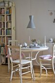 A coffee break on a white wooden table with wooden chairs and a 1950s-style pendant lamp hanging above
