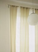 A detail of light fabric tab top curtains hung upon a metal curtain rod, hanging globe light