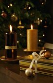 Burning candles with shiny and matte gold surfaces next to Christmas gifts