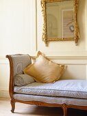 Backless sofa under gilt mirror in sitting room with white panelled walls.