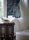 A detail of a traditional sitting room, ornate wooden side table, upholstered wing back armchair