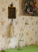 Blume in Glasflasche vor Wandtapete mit Blumenmuster