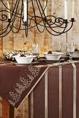 A Christmas table laid with a brown cloth with a wrought iron chandelier hanging above