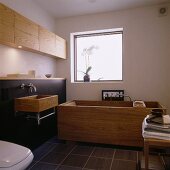 A designer bathroom with a cubic bathtub and a wooden wash basin against a black wall