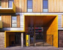 A modern apartment block with sliding wooden elements next to the windows and a yellow panelled entrance way