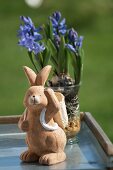 A clay rabbit figure in front of purple hyacinths in a glass