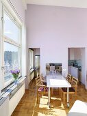 A long dining table with chairs in front of a window in a high ceilinged dining room