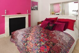 A double bed with decorative cushions and a quilt in a bedroom with pink and white walls