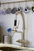Cups hanging from hooks above a kitchen tap