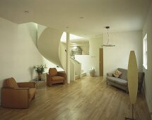Open modern living room with leather chairs in front of a winding staircase and designer floor lamps