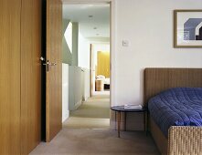 A bedroom with a double bed with a rattan headboard next to an open door with a view through the corridor into the guest bedroom