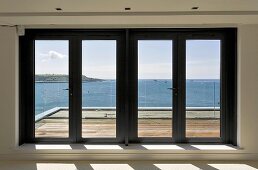 Terrassentüren aus Glas vor Holzterrasse mit Blick auf das Meer
