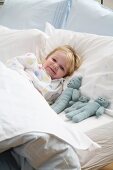 Little girl lying in bed with her plush animals