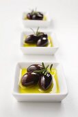 Schwarze Oliven mit Olivenöl und Rosmarin in Schälchen