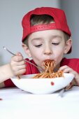 A little boy eating spaghetti with tomato sauce