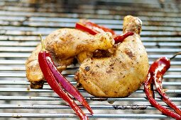Two chicken thighs with red chili peppers on a barbecue