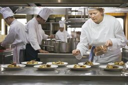 Female chef spooning sauce over main courses