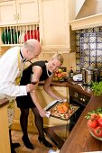Frau schiebt Ente in den Ofen, daneben Mann mit Rotweinglas