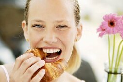 Junge Frau beisst lächelnd in ein Laugen-Croissant