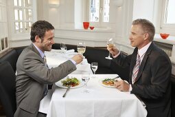 Zwei Männer mit Anzug sitzen im Restaurant beim Essen