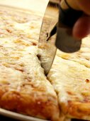 A Pizza Cutter Slicing Through a Cheese Pizza