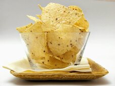 Tortilla Chips in a Glass Dish Resting on a Plate with Napkin