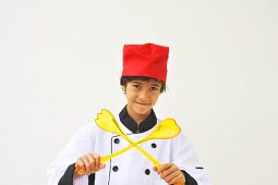A boy dressed as a chef holding salad servers