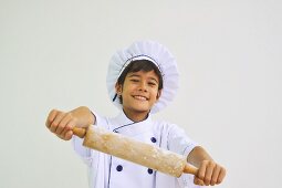 A boy dressed as a chef holding a rolling pin