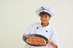 A boy dressed as a chef holding a pizza