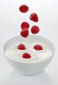 Raspberries falling into a bowl of yogurt