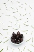 Kalamata olives in a bowl and scattered rosemary leaves