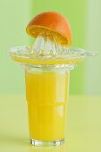A glass of orange juice, a juicer and an orange half