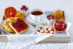 Frühstück im Bett mit Tee, Marmelade, Joghurt, Obst und Tomaten mit Mozzarella