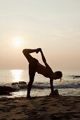 Frau praktiziert Yoga am Strand bei Sonnenuntergang