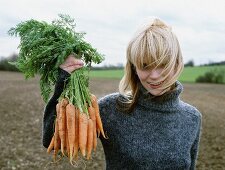 A woman proudly holding freshly harvested carrots