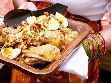 African woman holding bowl of chicken with peanuts & egg