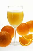 Kalter Orangensaft im Stielglas; Orangenschnitze und Orangen