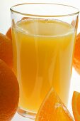 Orange juice in glass among oranges (close-up)