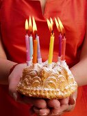 Hands holding small fruit cake with burning candles