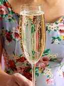 Frau in geblümtem Kleid hält Champagnerglas