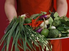 Woman holding plate of Asian vegetables, herbs etc