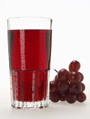 Glas roter Traubensaft mit Wassertropfen und rote Trauben
