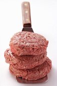 Three raw burgers in a pile on spatula