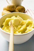 Mashed potato with butter in bowl with wooden spoon