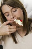 Young woman biting into piece of cream cake
