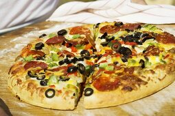 Person hält Pizza mit Peperoniwurst, Paprika und Oliven