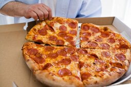 Hand taking piece of pepperoni pizza out of pizza box