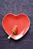 Strawberry on skewer on red heart-shaped plate