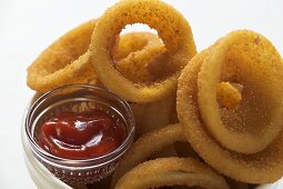 Deep-fried onion rings in white bowl, ketchup