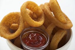 Deep-fried onion rings in white bowl, ketchup